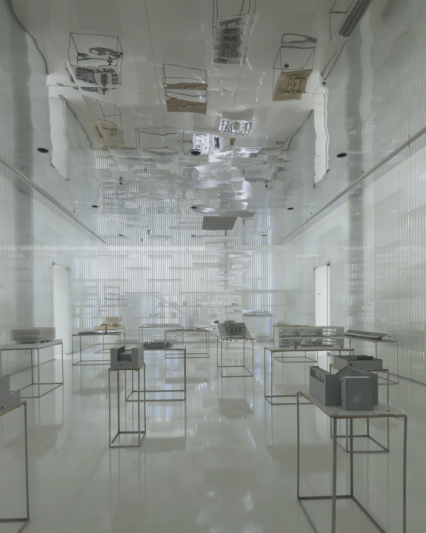 A quiet white gallery space with architectural models on display stands